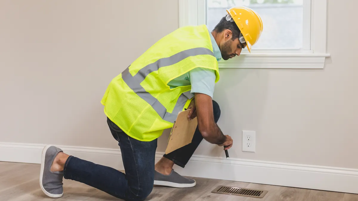 Worker checking a wall outlet near a floor vent