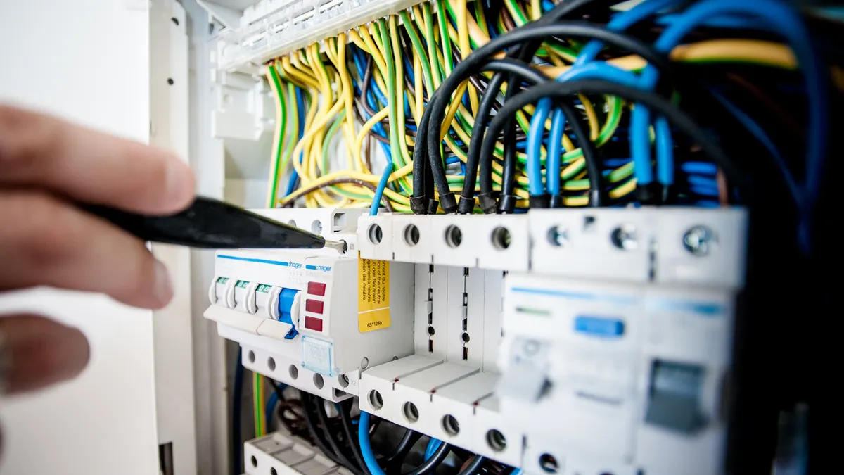 Open breaker panel with wiring and a hand pointing inside